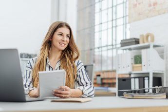 Young smiling woman holding notepad while sitting at desk in office